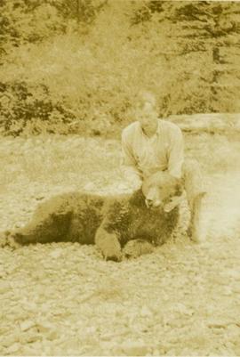 Kneeling man holding a dead bear