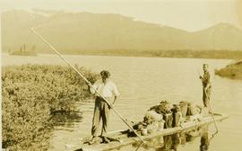 Two survey crewmen poling a raft laden with supplies along a lake