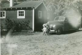 Two children pose in front of an automobile