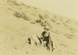 Joe Callao, rifle in hand, seated next to a felled big horn sheep