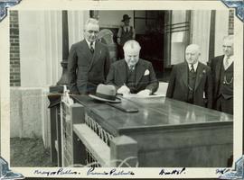 Harry Perry standing next to BC Premier Pattullo while he signs a document