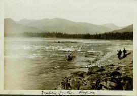 Men walking along a rocky river bank while a row boat is poled through Finlay Fork Rapids