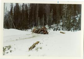 Arch-logging truck dragging a large load of logs uphill on a snowy road