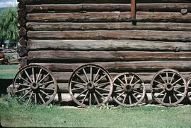Wagon wheels leaning on a log building at Father Pandosy Mission