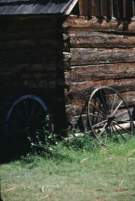 Wagon wheels leaning on a log building at Father Pandosy Mission