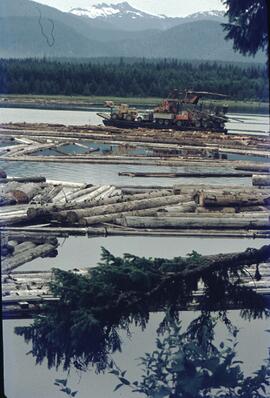 Boat carrying heavy logging equipment in booming area