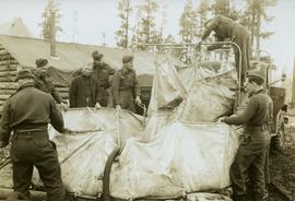 Soldiers transferring water from military truck water bag to a large water bag on the ground