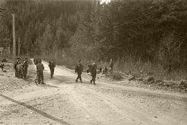Soldiers walking along road with children watching nearby