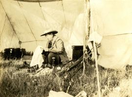 Harry Snyder sitting under a tent cleaning his rifle