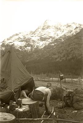 Two soldiers by tent with morning coffee, trying on snowshoes