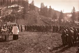 Military chaplain reading by a makeshift altar to a large group of soldiers