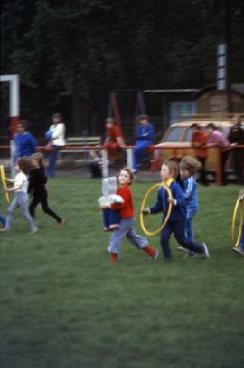 children running with a toy bear and hula hoops in East Germany