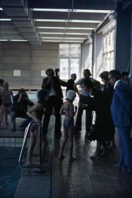 Iona Campagnolo interacting with a young female swimmer while standing in a group of unknown people at an aquatic centre in East Germany