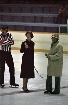 Iona Campagnolo speaking into microphone on Kitimat ice rink by hockey referee and man