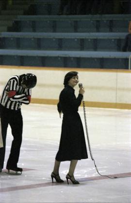 Iona Campagnolo speaking into microphone on Kitimat ice rink with hockey referee nearby