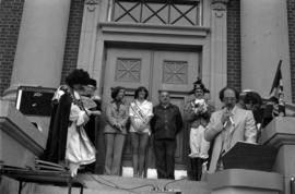 Iona Campagnolo, Miss Prince Rupert, and Mayor Peter Lester behind announcer at door of Prince Rupert courthouse