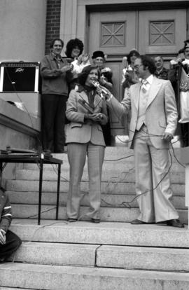 Iona Campagnolo speaking into microphone in front of Prince Rupert courthouse with Miss Prince Rupert and Mayor Peter Lester