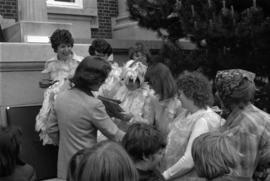 Iona Campagnolo shaking hands with a group of women dressed in chicken costumes in front of Prince Rupert courthouse