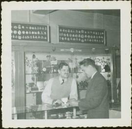 James Joseph Claxton and an unidentified man conversing over the jewelry counter at at of Roderick Jewelers, New Westminster