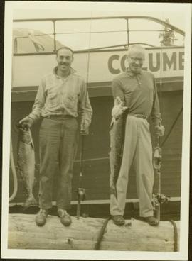 Two fishermen pose for a photo in front of the boat Columbia