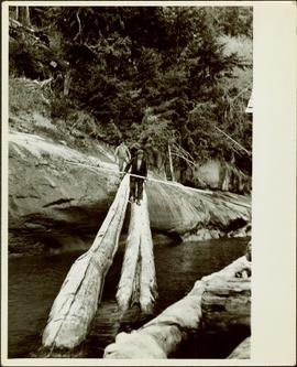 Two men walking across a large log over water at Knight Inlet