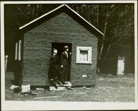 A priest and a man standing in the doorway of a small house under construction