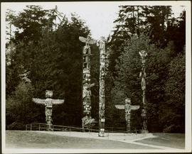 Five totem poles of various sizes standing within a fenced enclosure