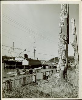A man in uniform and a woman pose for a photo beside totem poles