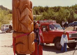 Woman in button blanket standing beside totem pole at opening of Haisla Recreation Centre in Kitamaat Village