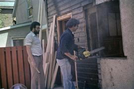 Assistant to Iona Campagnolo and man with chainsaw work on a window frame in a house under construction