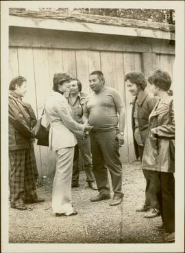 Iona Campagnolo shaking hands with an unidentified First Nations man in front of a longhouse whil...