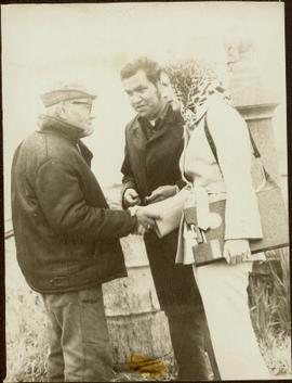 Iona Campagnolo holding a clipboard and shaking hands with an unidentified man while another man looks on