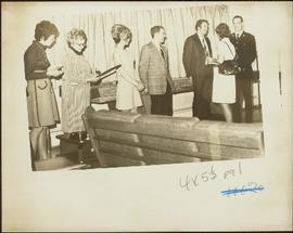 Three unidentified women and three unidentified men stand in a line in a curtained room as Iona Campagnolo talks to one of the men