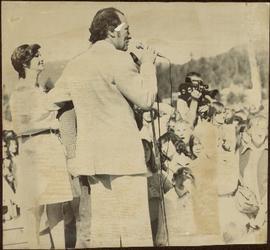 Pierre Trudeau speaks to crowd, arm around unidentified man, and Iona Campagnolo behind him