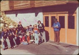 Minister Iona Campagnolo and unidentified man speak to group of eighteen boys in front of the Terrace Hockey School, summer 1977