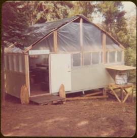 Temporary cabin built with 2x4s, tar paper, and plastic sheeting and marked “Iona Hall,” summer 1977