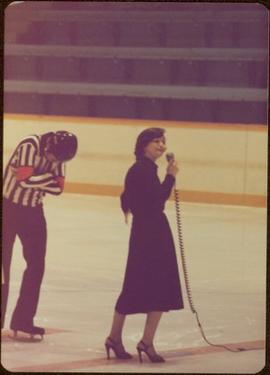 Minister Iona Campagnolo speaking into microphone on ice, with referee in background