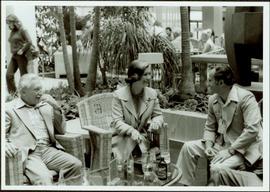 Johnny Esau, Iona Campagnolo, and George Gross sit around patio table in Vienna, European Sports Tour, 1977