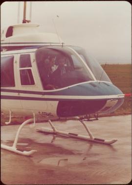 Iona Campagnolo sitting in copilot seat next to unidentified pilot in helicopter on landing strip