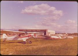 Skeena Riding tour - Small aircraft and gliders lined up in front of building labeled “British Columbia Forest Service”