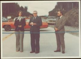 Minister Iona Campagnolo stands next to two unidentified men behind blue ribbon at the opening of Scott Road to Fairview Terminal, Prince Rupert