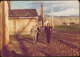 Iona Campagnolo and several unidentified others walk past totem poles and longhouses at 'Ksan, BC