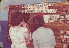 Three unidentified women, one of whom may be Iona Campagnolo, look at a picture board entitled “Discover Gardening with the Prince Rupert Garden Club”