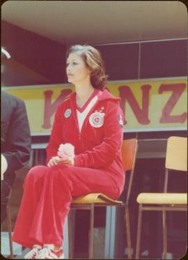 Iona Campagnolo sits on a chair in a jogging suit, holding a rose, Kitimat, BC