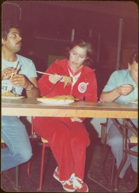 Iona Campagnolo sits on a chair in a jogging suit, eating chow mein with chop sticks at cookoff i...