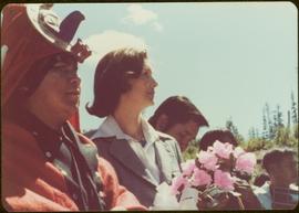 Holding a bouquet of pink silk roses, Iona Campagnolo stands next to an unidentified man in dancing regalia, Kitimat, BC