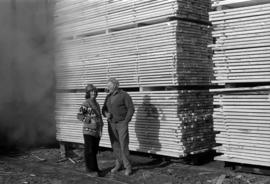 Iona Campagnolo with hard hat speaking with man in front of wood at sawmill owned by Rim Forest P...