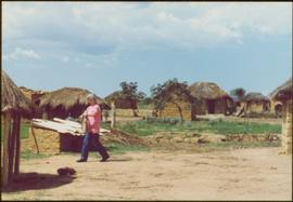 CUSO Mission in Angola - Iona Campagnolo walking on path between thatched-roof huts