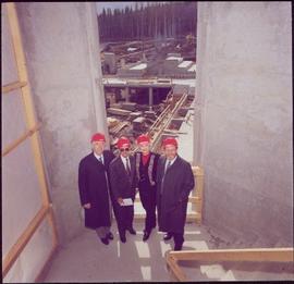 Murray Sadler, John Backhouse, Iona Campagnolo, and Geoffrey R. Weller pose with hardhats in a stairwell during the construction of UNBC