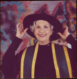 Portrait of Iona Campagnolo in regalia, smiling as she pulls on her Chancellor’s hat